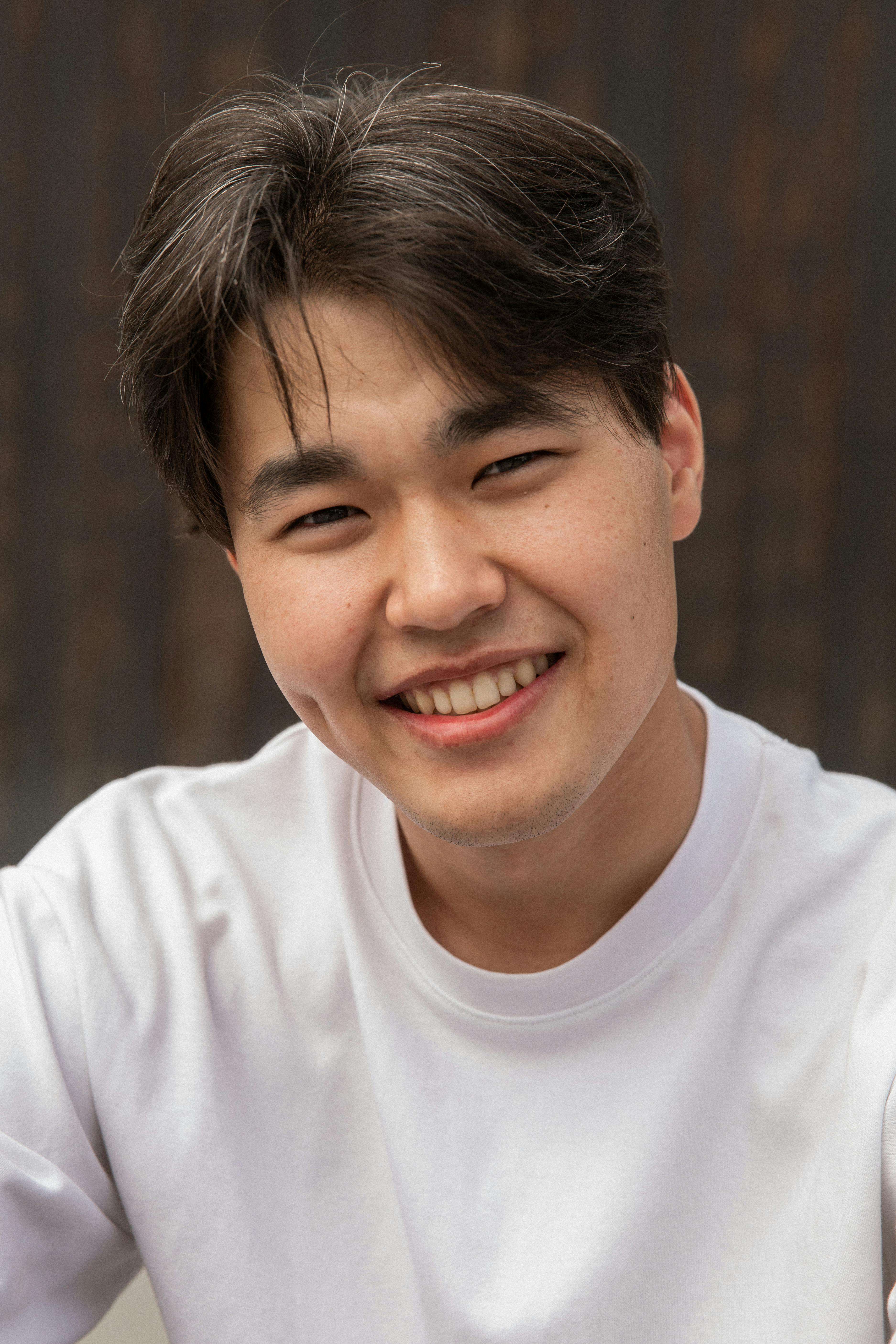 Smiling Asian man in a white sweater looking at the camera with a joyful expression. He has dark hair.
